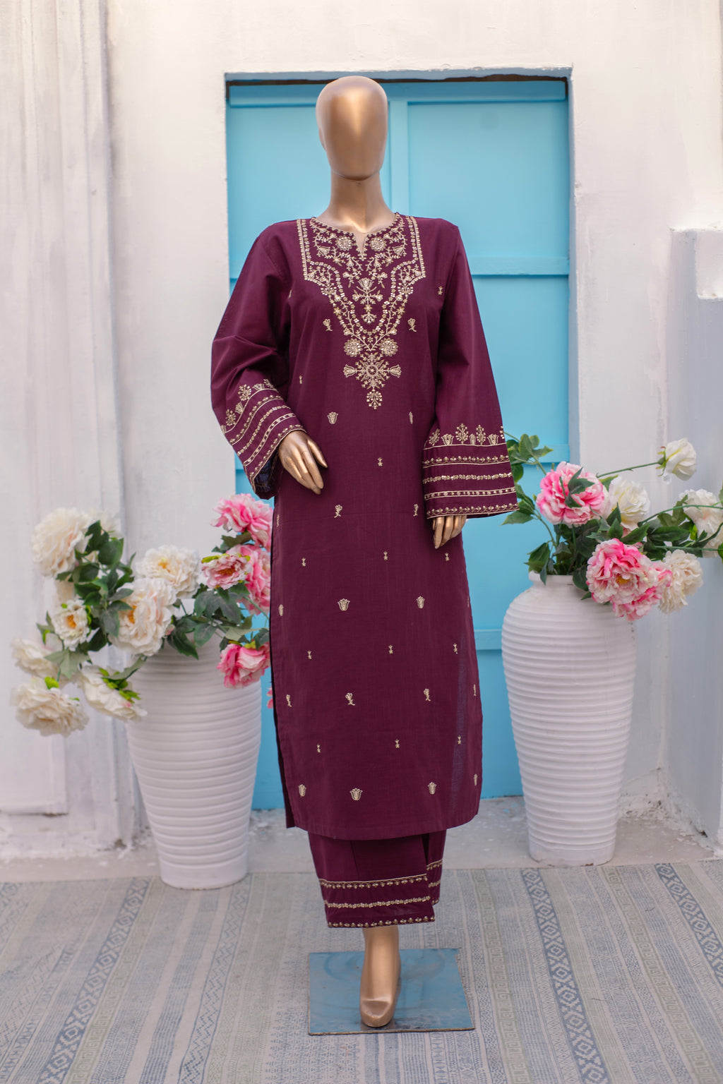 Mannequin wearing a maroon embroidered outfit with flowers and a blue door in the background