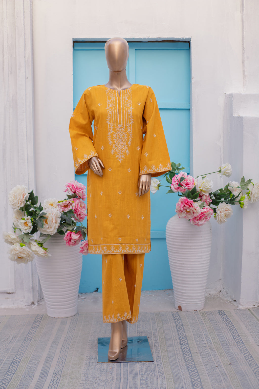 Yellow embroidered traditional outfit on a mannequin with floral decorations in a room.